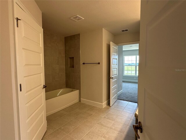 bathroom with tile patterned flooring, tiled shower / bath combo, and a textured ceiling