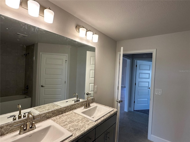 bathroom with a textured ceiling, vanity, and tiled shower / bath combo