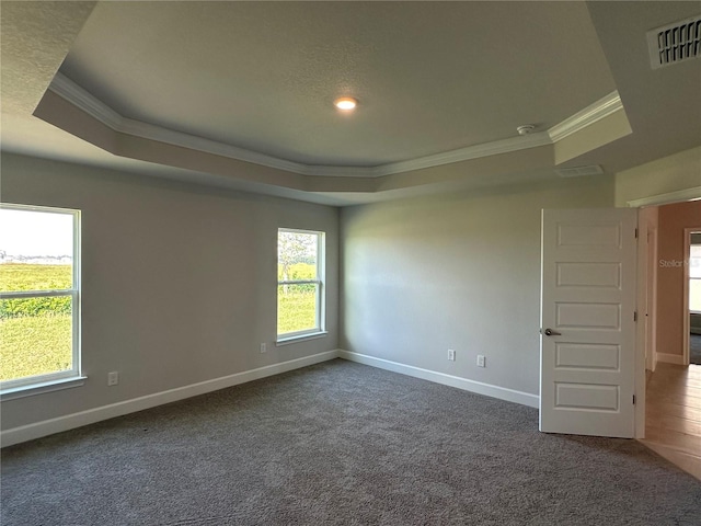 unfurnished room featuring crown molding, a wealth of natural light, a tray ceiling, and dark carpet