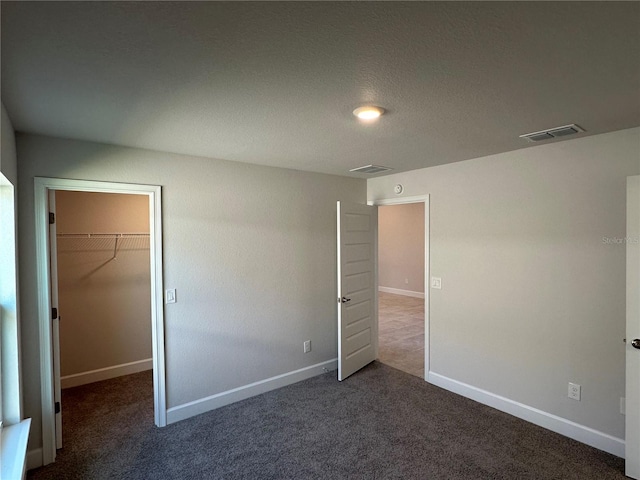 unfurnished bedroom with dark colored carpet, a spacious closet, and a closet