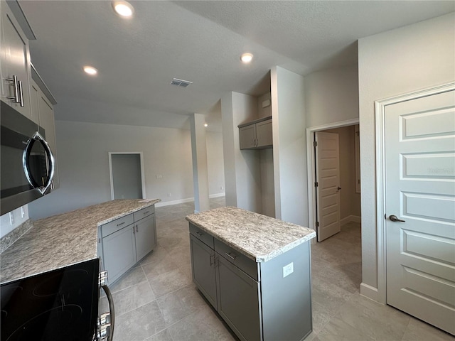 kitchen featuring gray cabinets, stove, a textured ceiling, and a kitchen island