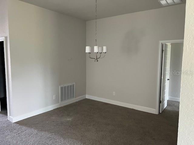 empty room with dark carpet and a chandelier