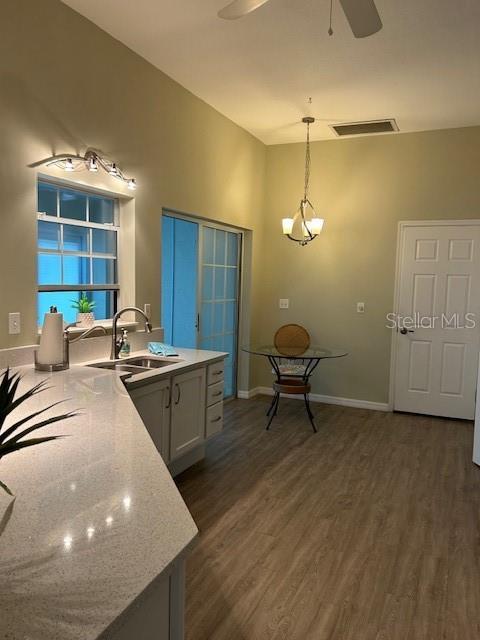 kitchen with sink, white cabinetry, dark hardwood / wood-style flooring, pendant lighting, and ceiling fan with notable chandelier