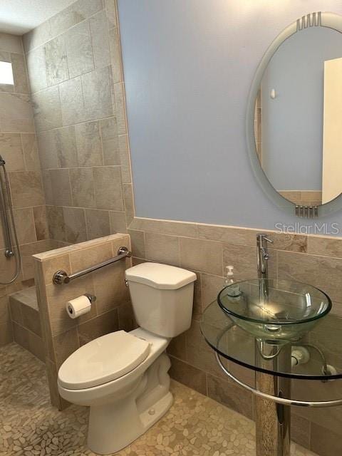 bathroom featuring a tile shower, sink, tile walls, toilet, and tile patterned floors