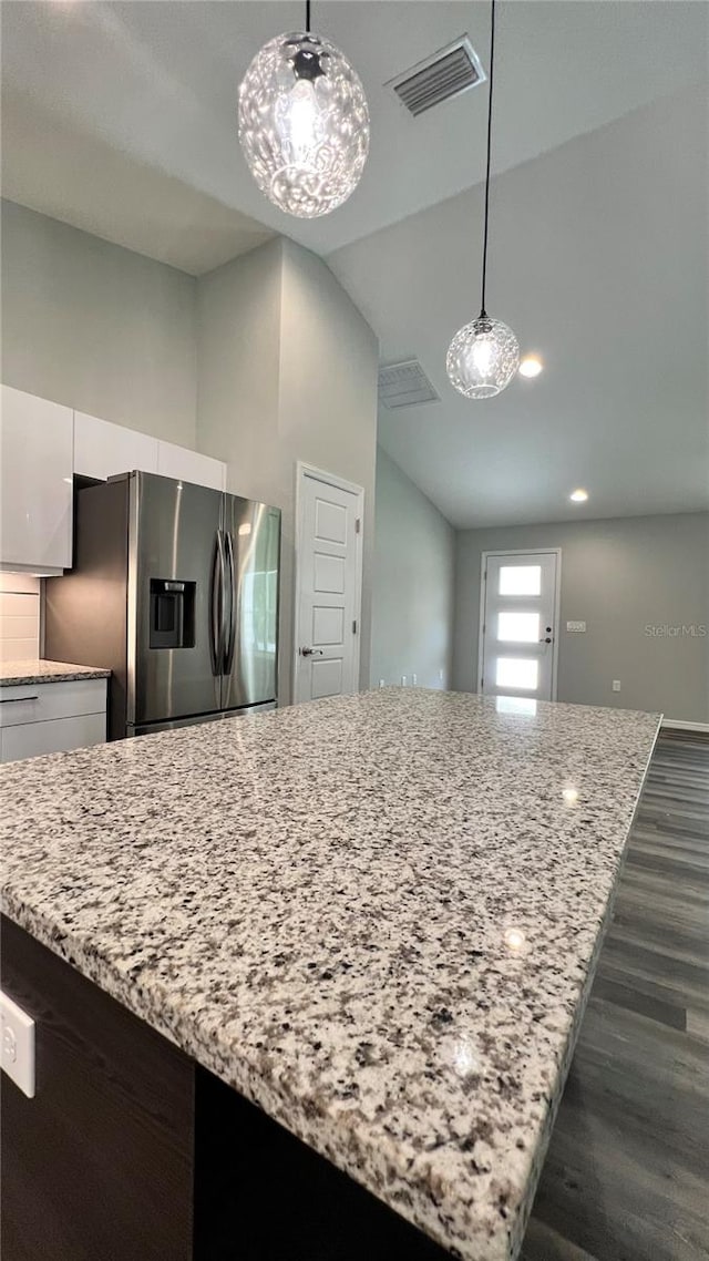 kitchen featuring hanging light fixtures, light stone countertops, stainless steel fridge, dark wood-type flooring, and white cabinets