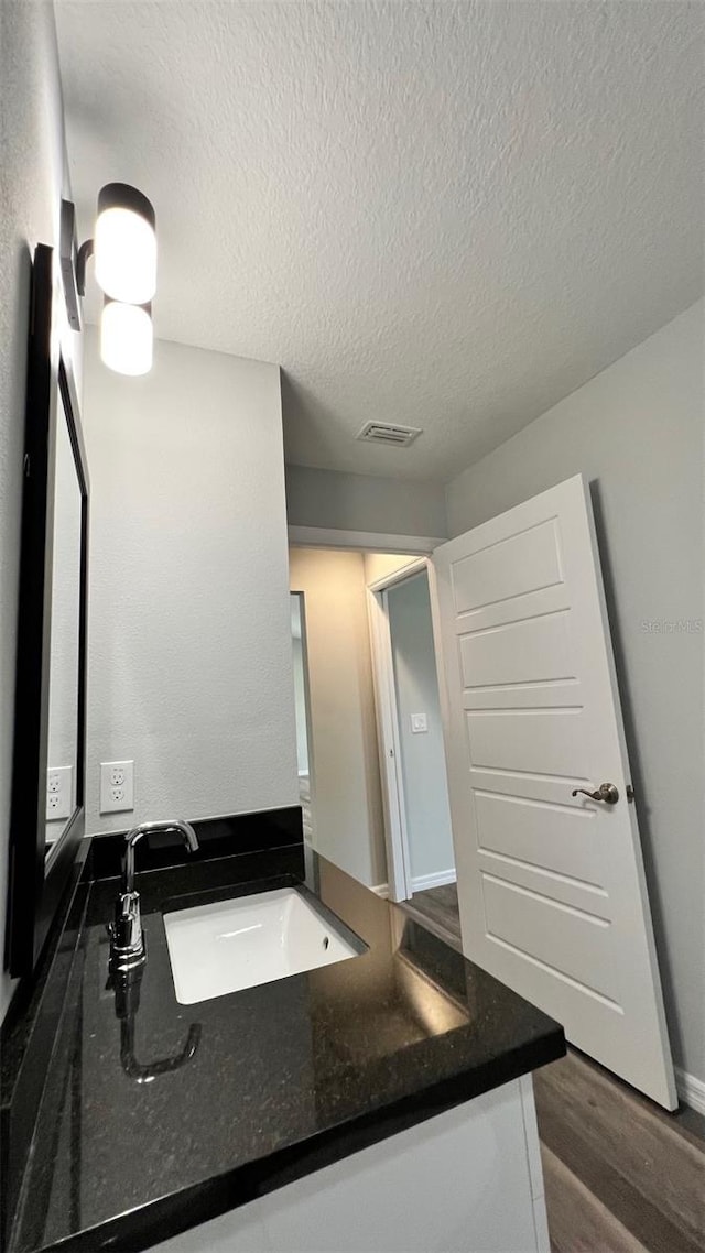 bathroom with a textured ceiling, wood-type flooring, and vanity