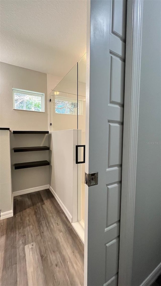 full bathroom with baseboards, a textured ceiling, wood finished floors, and walk in shower