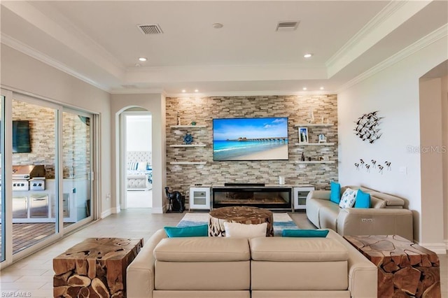 living room featuring a tray ceiling, a fireplace, and crown molding