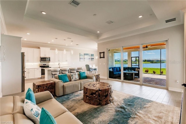 living room with a tray ceiling, ceiling fan, and a water view