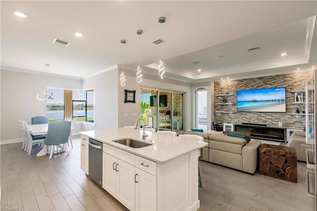 kitchen featuring white cabinetry, a center island with sink, stainless steel dishwasher, a tray ceiling, and pendant lighting