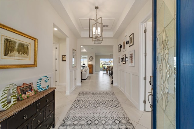 hallway with a raised ceiling, light tile patterned floors, and an inviting chandelier