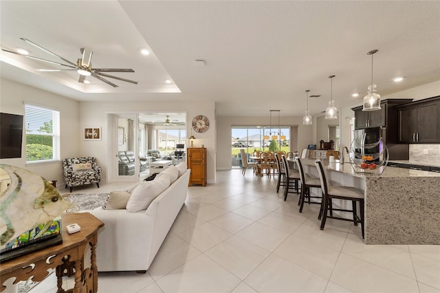 tiled living room with ceiling fan and a raised ceiling