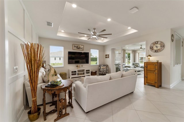 tiled living room featuring ceiling fan and a tray ceiling