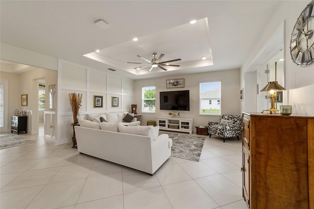 tiled living room with ceiling fan and a tray ceiling