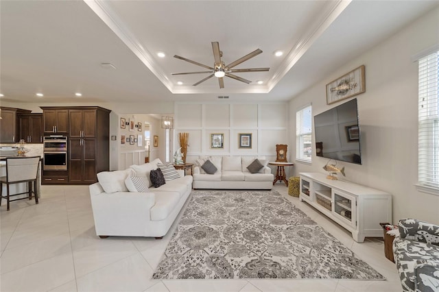 living room with a raised ceiling, ceiling fan, crown molding, and light tile patterned flooring