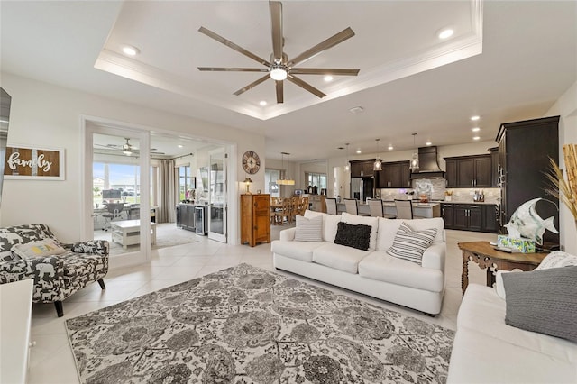 tiled living room featuring a tray ceiling, ceiling fan, and crown molding