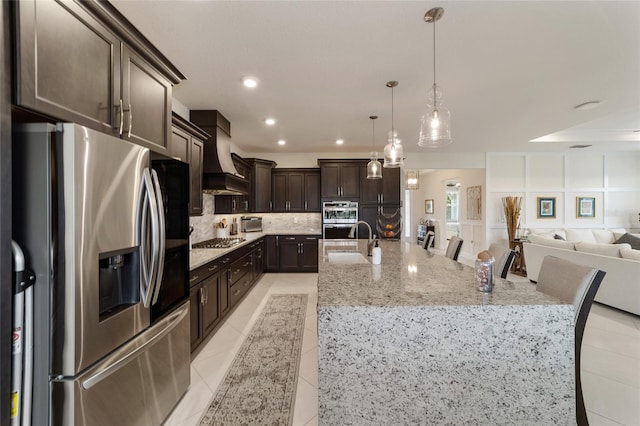 kitchen with a large island with sink, appliances with stainless steel finishes, a kitchen bar, and custom range hood