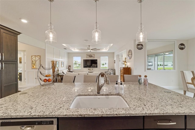 kitchen with pendant lighting, dark brown cabinets, light stone counters, and sink