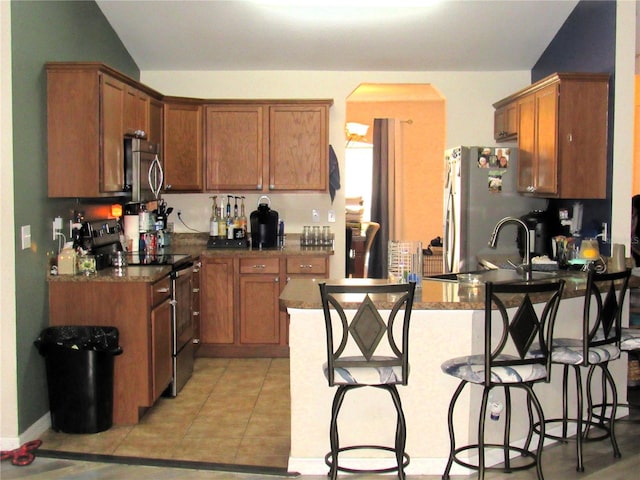 kitchen featuring light tile patterned floors, arched walkways, a peninsula, stainless steel appliances, and a kitchen bar