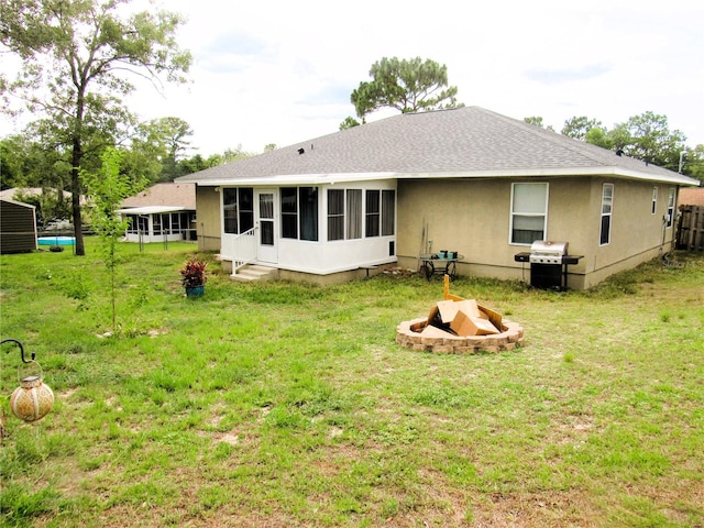 rear view of house featuring a fire pit, a lawn, a sunroom, and stucco siding