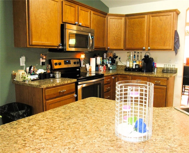 kitchen featuring brown cabinets, light stone counters, and stainless steel appliances