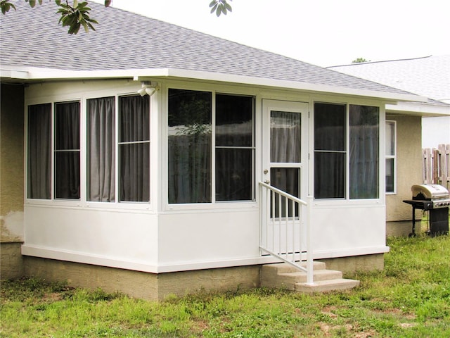 view of side of home featuring a sunroom, a shingled roof, and stucco siding