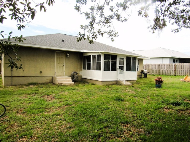 rear view of property with a shingled roof, a lawn, entry steps, a sunroom, and fence