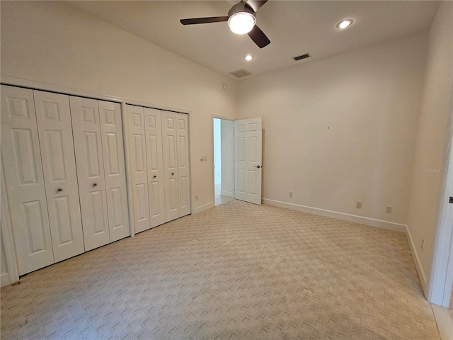 unfurnished bedroom with light colored carpet, ceiling fan, and multiple closets