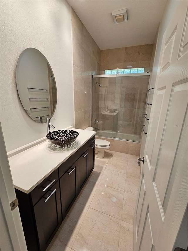 full bathroom with tile floors, bath / shower combo with glass door, vanity, and toilet