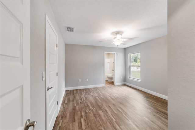 unfurnished bedroom with wood finished floors, a ceiling fan, visible vents, baseboards, and ensuite bath