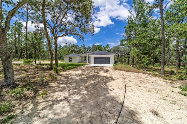 view of front of house featuring an attached garage, dirt driveway, and stucco siding