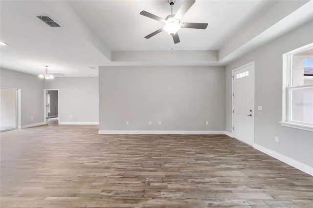 empty room featuring visible vents, baseboards, wood finished floors, and ceiling fan with notable chandelier