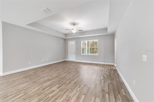 spare room featuring visible vents, a tray ceiling, baseboards, and wood finished floors