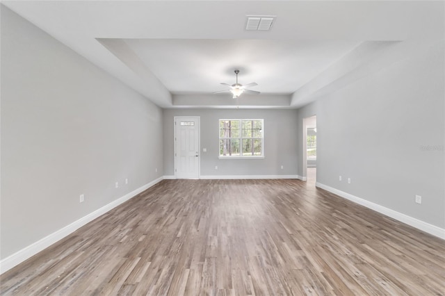 unfurnished living room with visible vents, baseboards, a ceiling fan, a raised ceiling, and wood finished floors