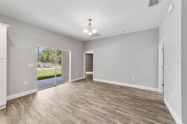 empty room featuring baseboards, wood finished floors, visible vents, and an inviting chandelier