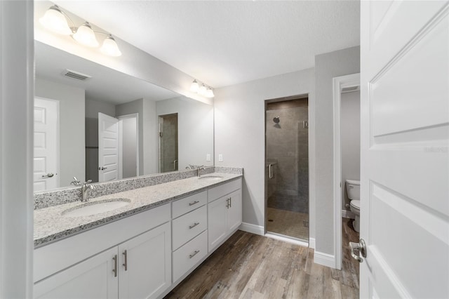 full bathroom featuring wood finished floors, a sink, visible vents, and a shower stall