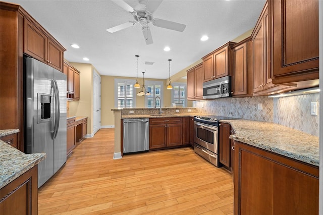 kitchen featuring hanging light fixtures, appliances with stainless steel finishes, backsplash, and light wood-type flooring