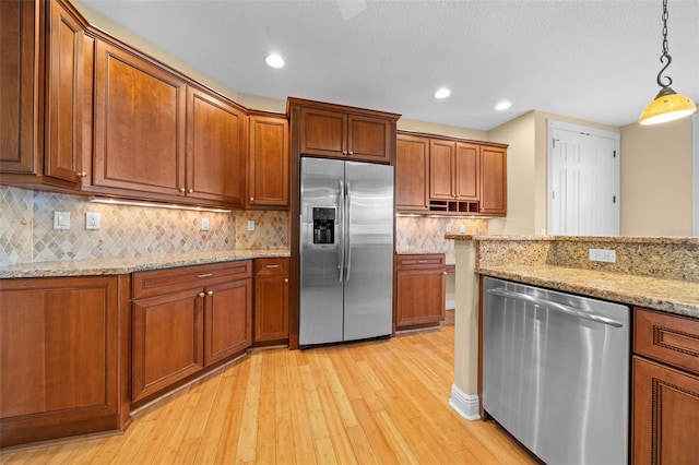 kitchen featuring light hardwood / wood-style flooring, light stone counters, pendant lighting, and appliances with stainless steel finishes