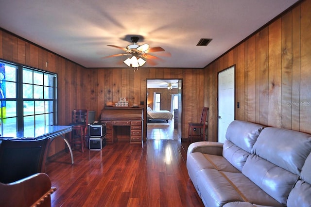 living room featuring ornamental molding, wooden walls, dark hardwood / wood-style floors, and ceiling fan