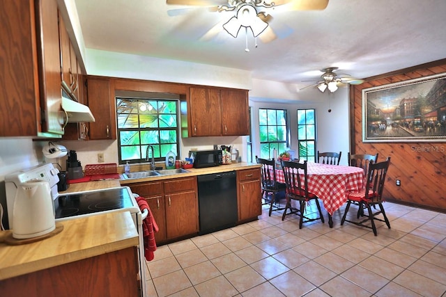 kitchen with wood walls, black appliances, sink, ceiling fan, and light tile patterned floors