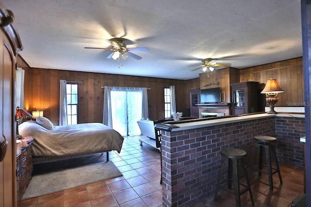 tiled bedroom featuring ceiling fan, a textured ceiling, access to exterior, wood walls, and a fireplace