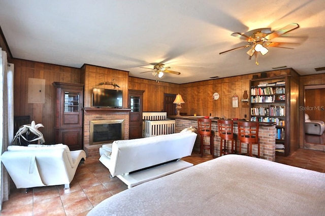 living room with ceiling fan, wooden walls, a fireplace, and bar area