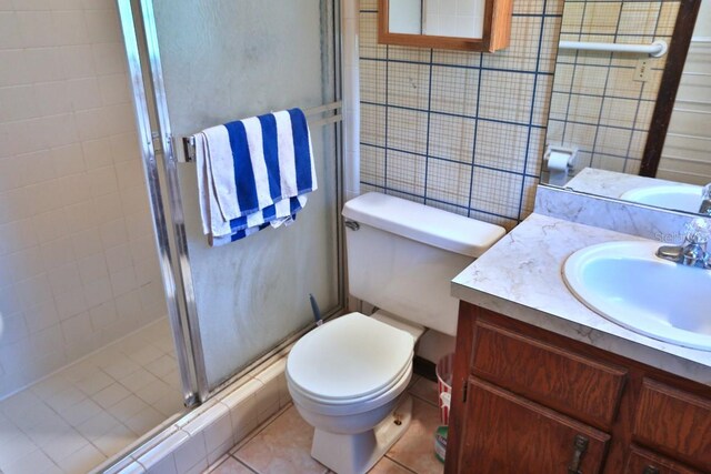 bathroom featuring a shower with door, vanity, toilet, and tile patterned flooring