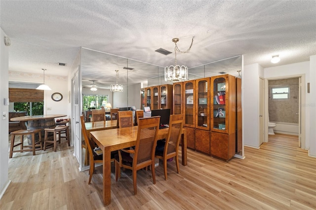 dining space with light hardwood / wood-style flooring, ceiling fan with notable chandelier, and a textured ceiling