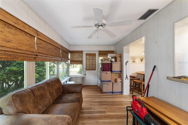 living room with light hardwood / wood-style flooring, ceiling fan, and wooden walls