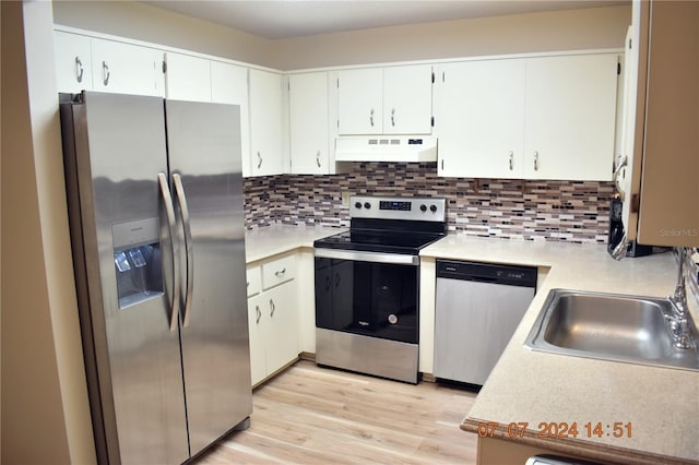 kitchen with white cabinets, sink, decorative backsplash, light wood-type flooring, and appliances with stainless steel finishes