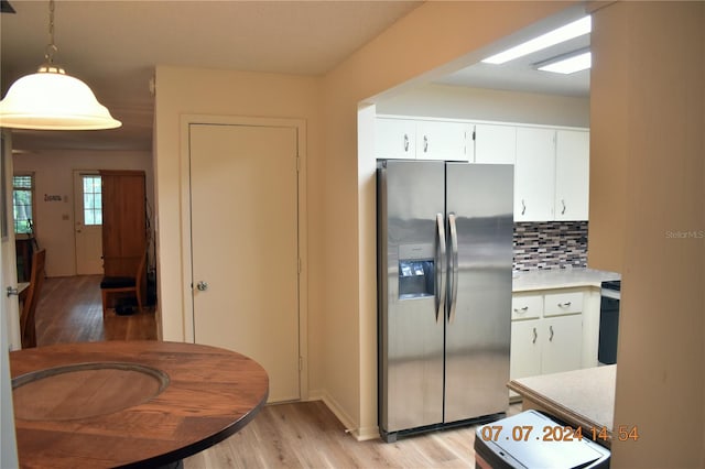 kitchen featuring white cabinetry, stainless steel refrigerator with ice dispenser, backsplash, pendant lighting, and light hardwood / wood-style floors