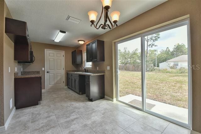 kitchen with dark brown cabinetry, sink, light tile patterned flooring, and a notable chandelier