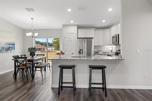 kitchen with kitchen peninsula, light stone counters, stainless steel appliances, an inviting chandelier, and white cabinetry