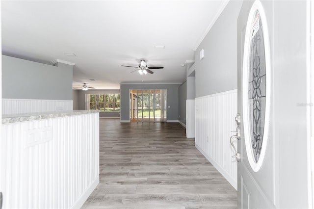 foyer entrance featuring ornamental molding, light wood-type flooring, wainscoting, and a ceiling fan